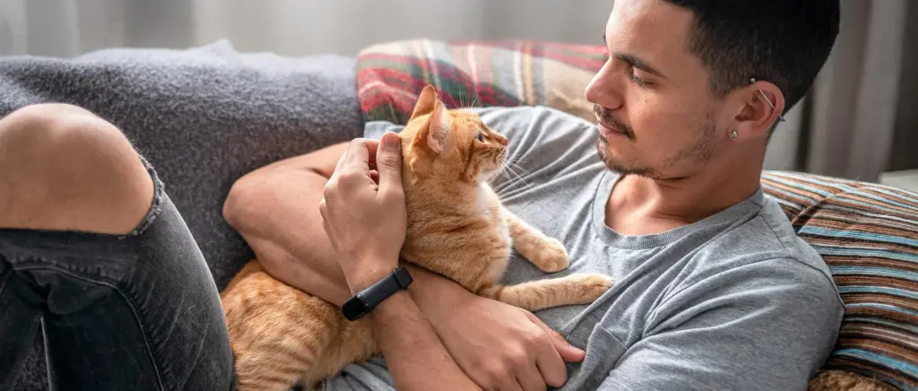 A man cuddling an orange cat on the couch